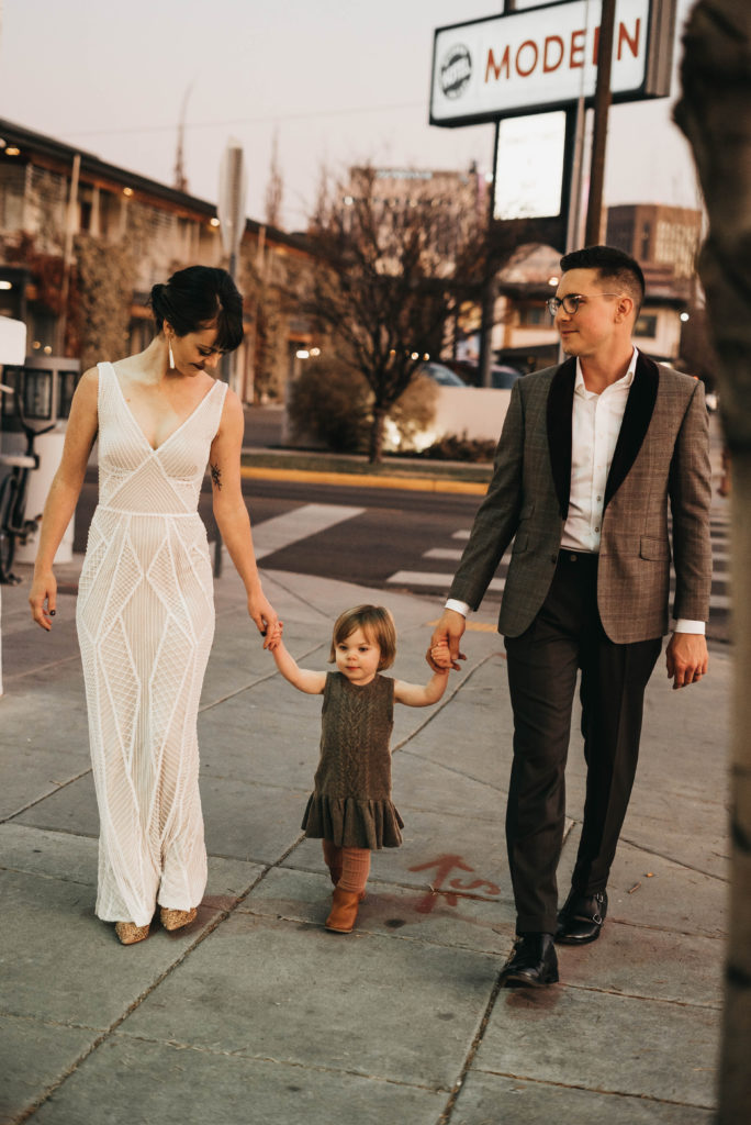 couple walks with their daughter outside of the linen building with the modern hotel in the background