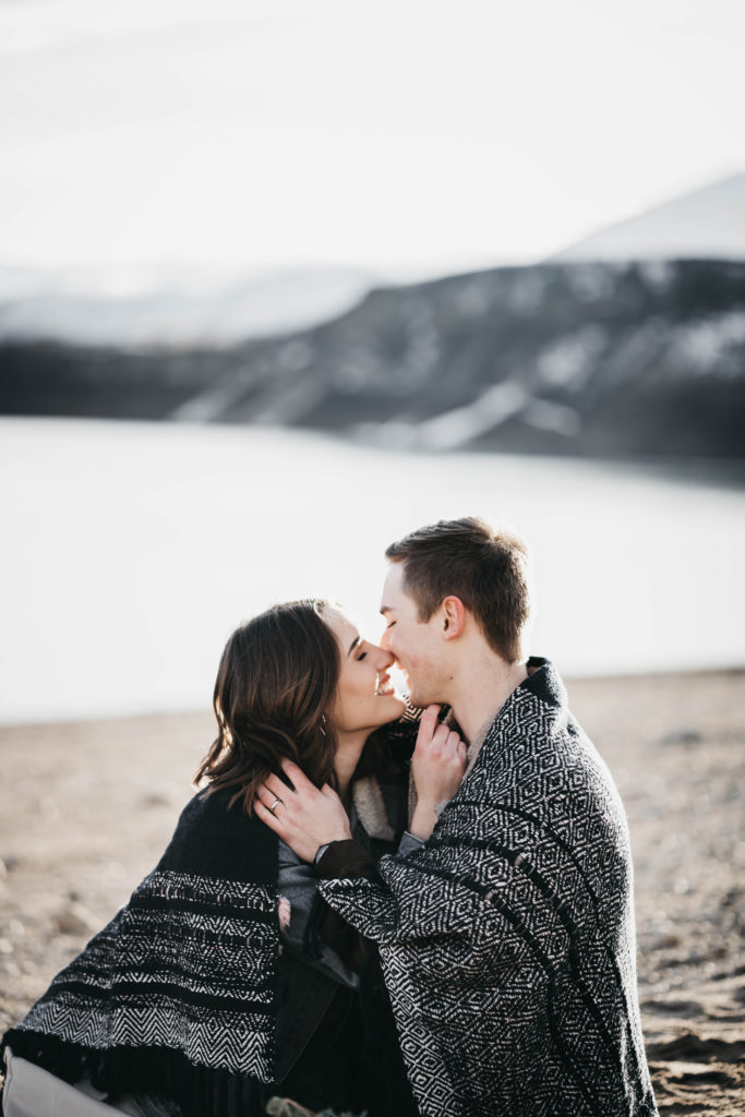on the beach of lucky peak lake newlywed couple cuddles in a blanket together
