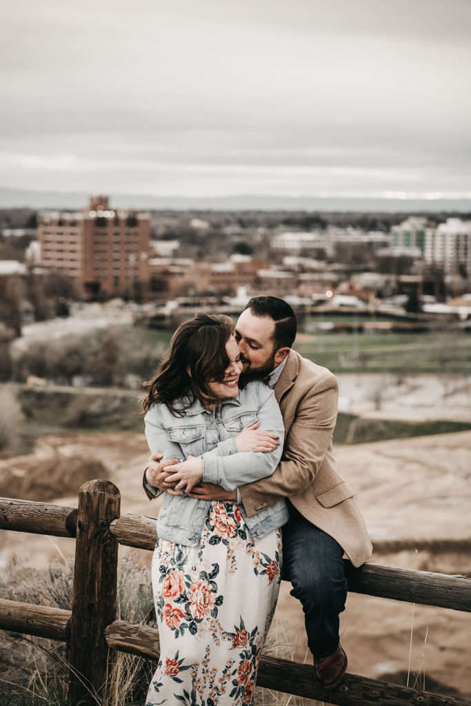 Couple cuddles close together in the wind during their engagement session at the military reserve