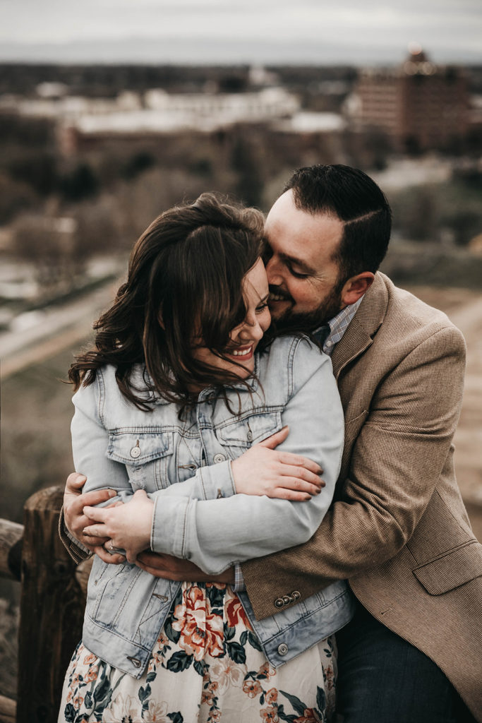 wind blows through the couple's hair as they cuddle up together during their engagement session