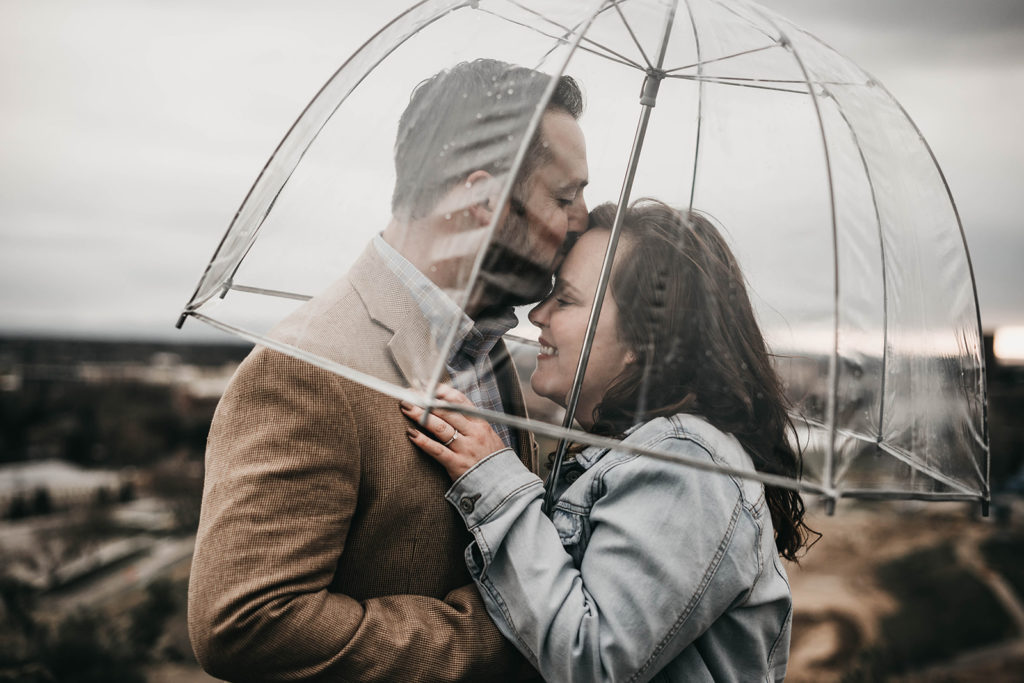 couple cuddles under a clear umbrella during their engagement session