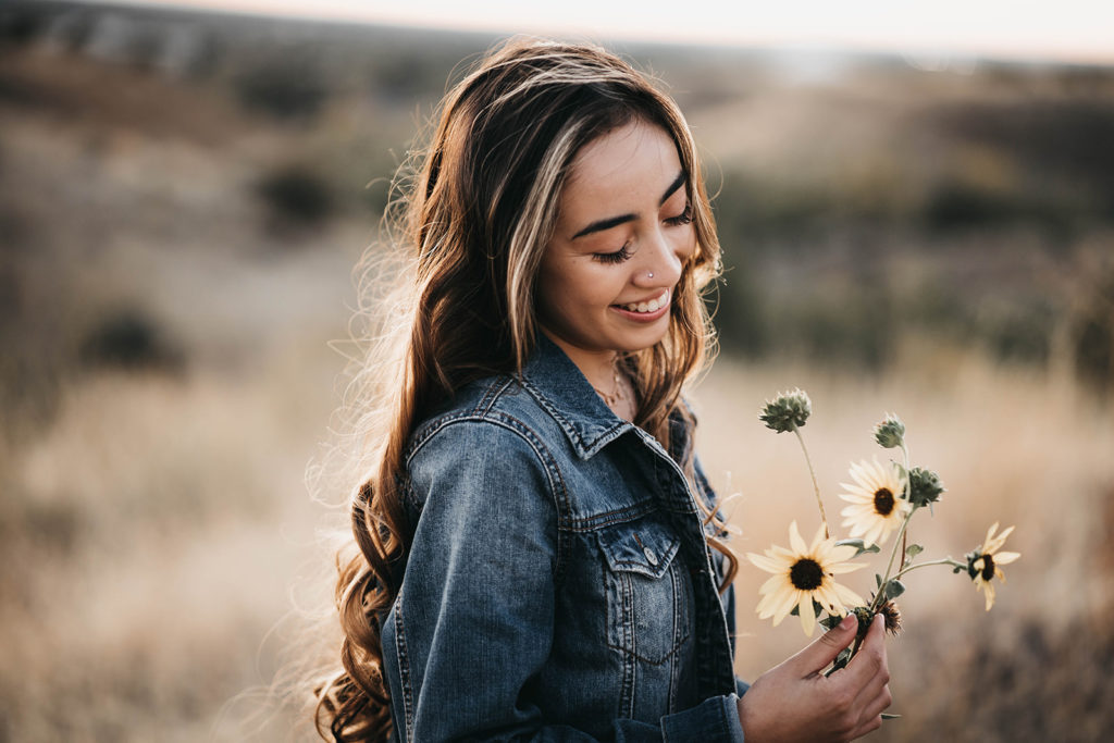 high school senior smiles down at the boise foothills sunflowers she is holding during her senior session