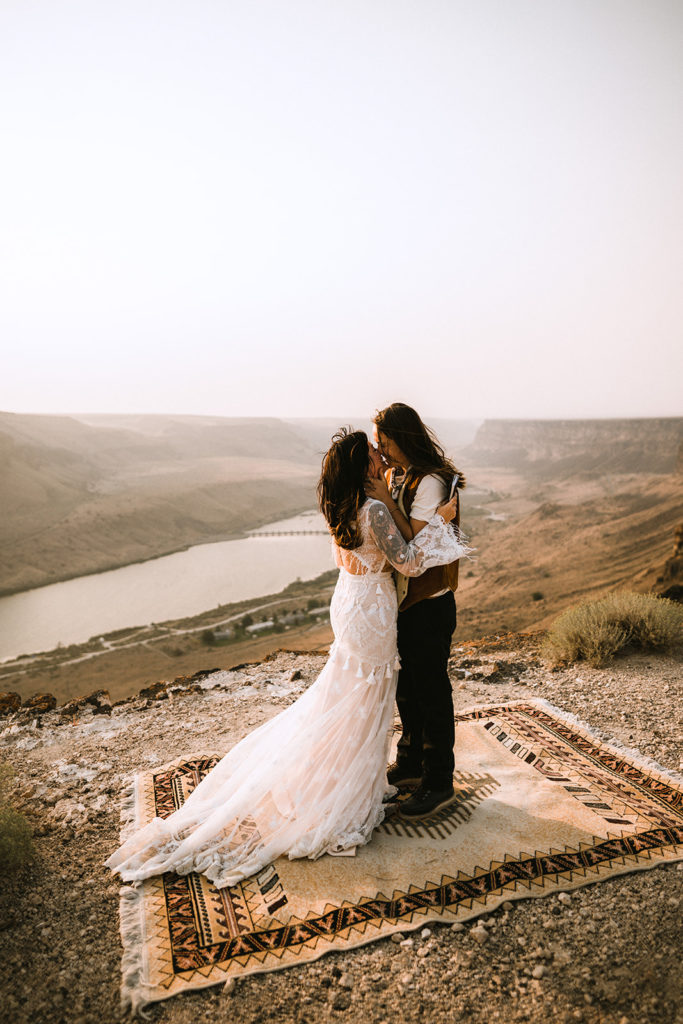 Brides share their first kiss as the sunsets over the desert canyon
