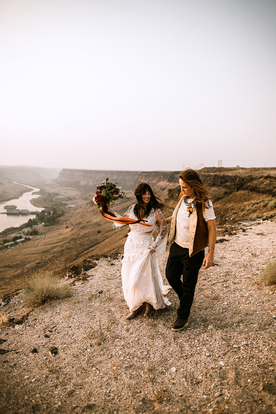 Brides walk together along the edge of the snake river canyon holding a bouquet