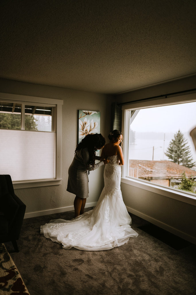bride in front of the window getting her dress buttoned up