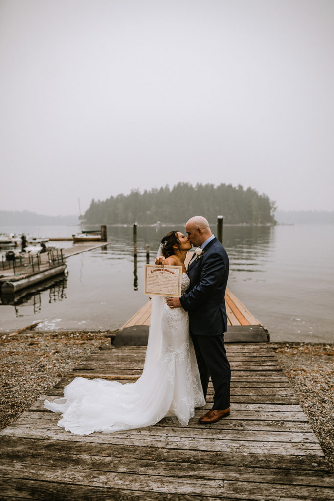 Newlyweds holding up their marriage certificate standing on the beach of a lake in Tacoma, Washington