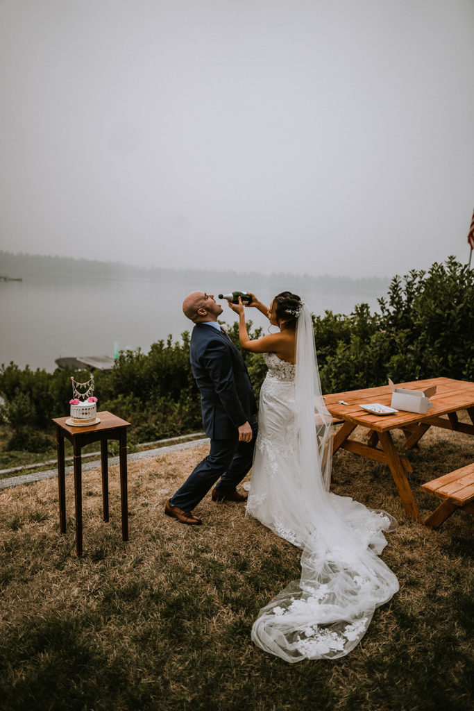 Groom kneels down so his bride can give him a sip of champagne from the bottle during their elopement