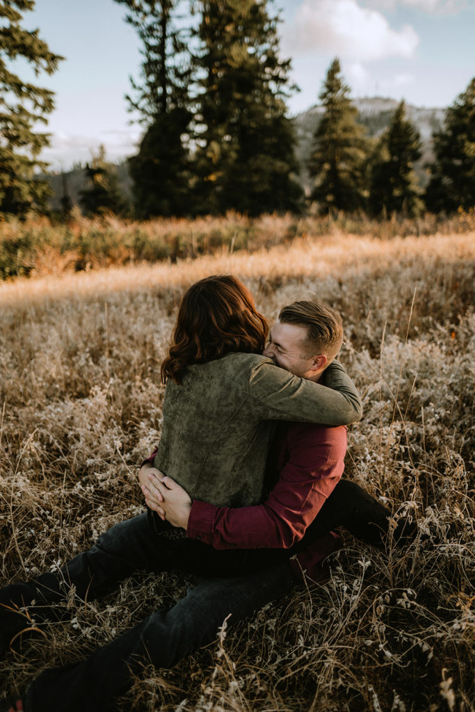 couple laughs together while cuddling in a field during their Bogus Basin couple session