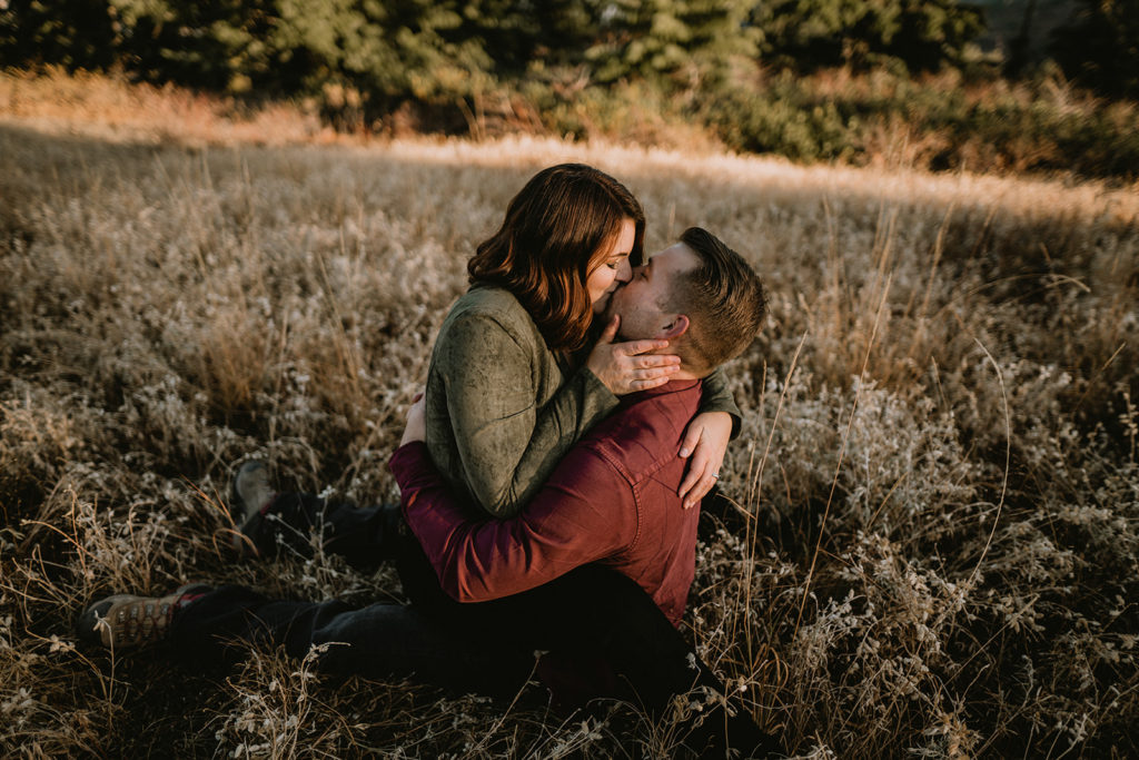 Couple kissing while sitting in a mountain field during their Bogus Basin couple session