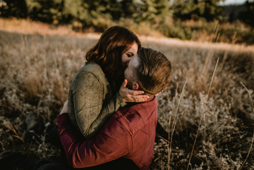 couple kisses each other while sitting together in a field during their Bogus Basin couple session