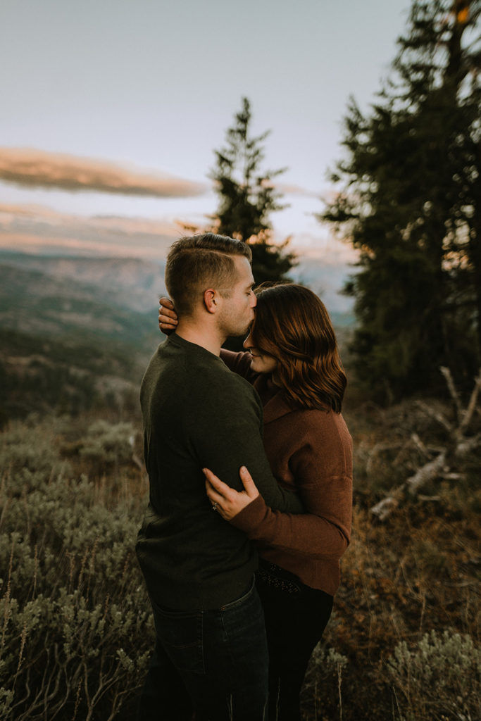 husband kisses wife's forehead as the sun sets over the mountains during their Bogus Basin couple session