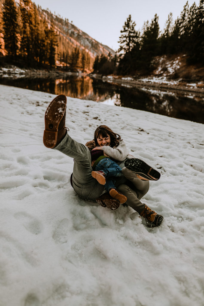 family tumbles on the snow together with a river in the background