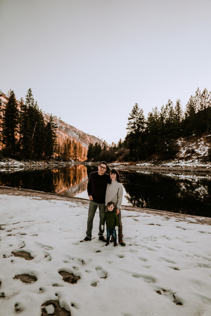 cute family poses for a family photo in front of the Payette River during their family session
