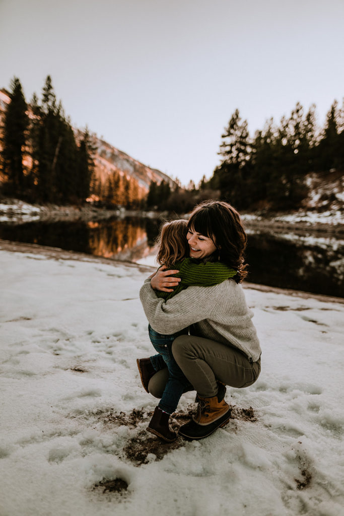 girl gives her mother a hug with the sunset and river behind them