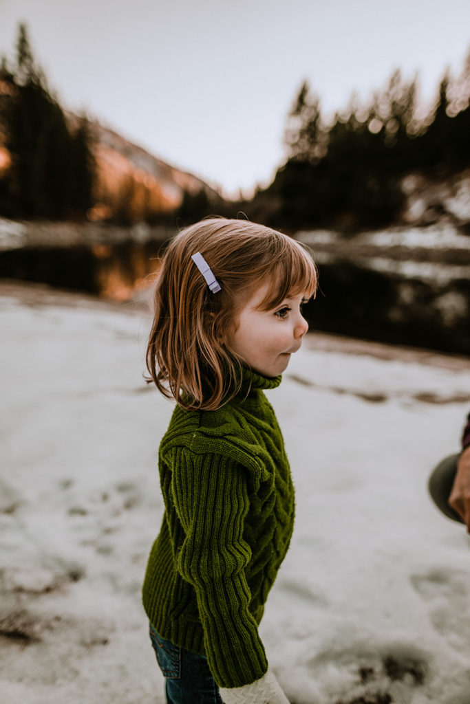little girl stands looking at her mother off screen while standing on the banks of the Payette River