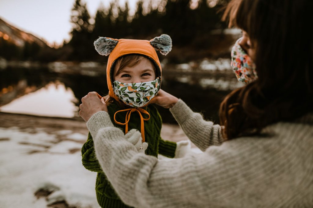 mother adjusts her daughters face mask during their Payette River family session