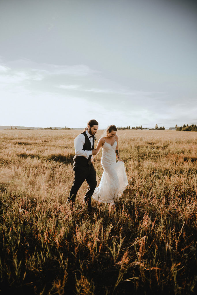Bride and groom run through a pasture hand in hand as the sun sets during their wedding reception in donnelly, idaho.
