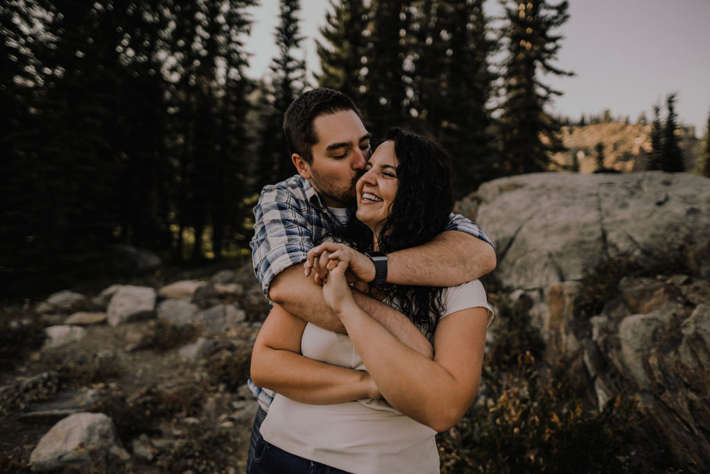 couple embraces as man kisses his fiancee on the cheek during their Blue Lake engagement session in Cascade, Idaho