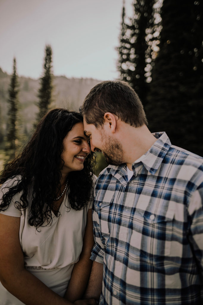 couple leans together and touches foreheads together with the sun and mountains in the background