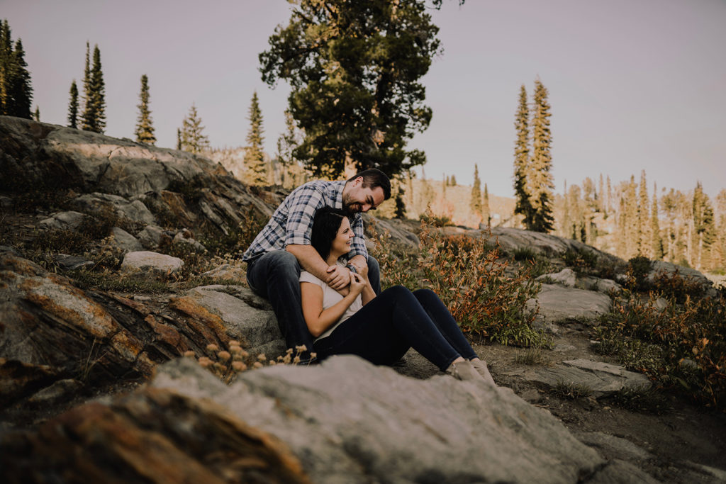 Couple sits together on a rock embracing during their Blue Lake engagement session in Cascade, Idaho