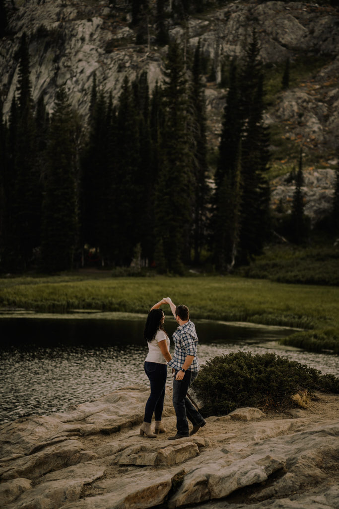 couple dances together as they overlook the mountain lake and trees during their Blue Lake engagement session