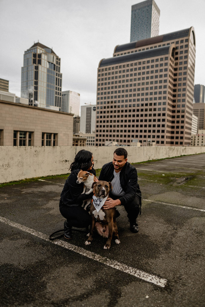 Engaged couple on a Seattle rooftop parking garage with their two dogs during their city engagement session