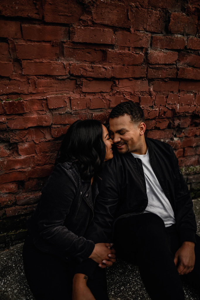 cute couple laughs together in front of a red brick wall during their downtown Seattle engagement session