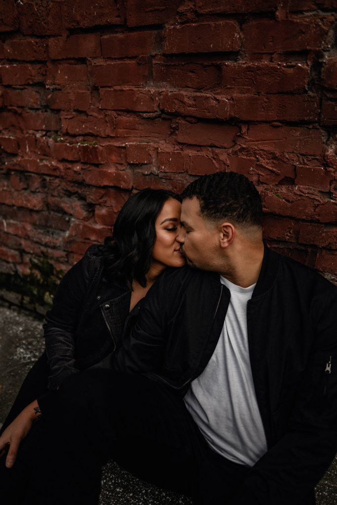couple sitting in front of a brick wall during their downtown Seattle engagement session