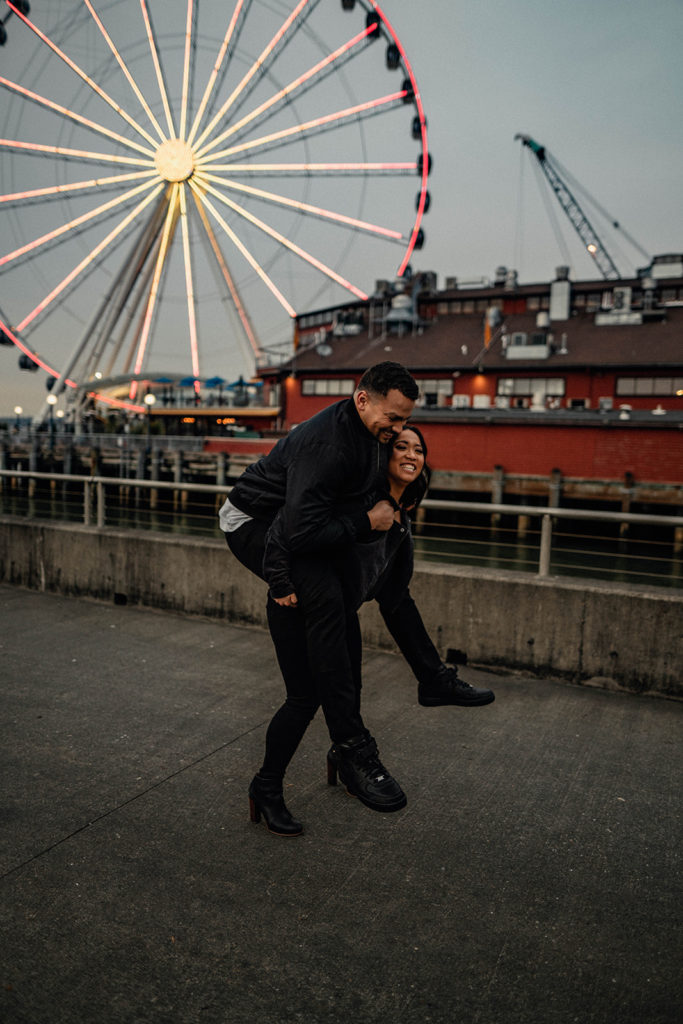 couple goofing off with a piggyback ride during their engagement session at the seattle great wheel