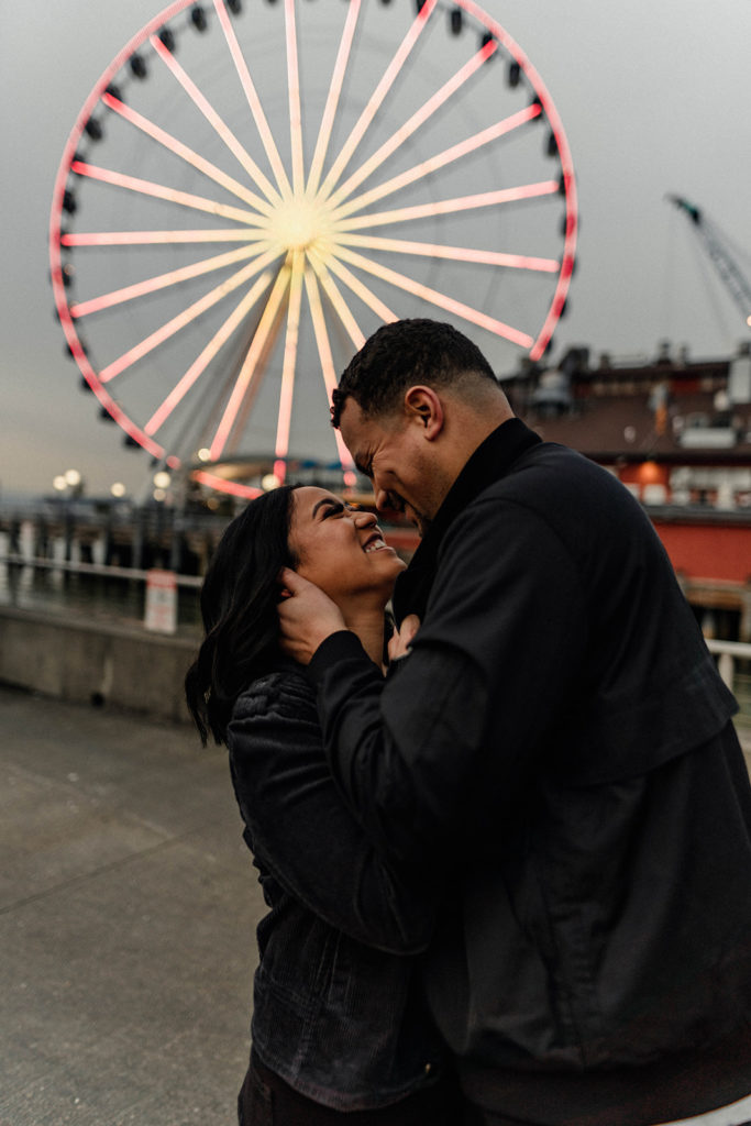 couple enjoys their engagement session on a pier in front of a Ferris wheel