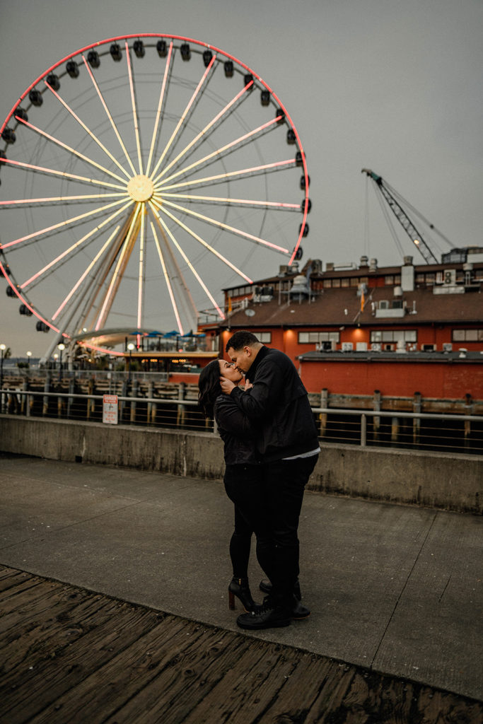 couple kisses in front of a ferris wheel during their engagement session
