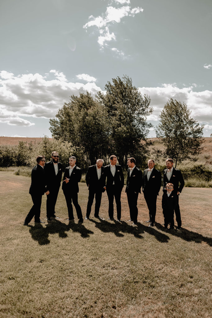 groomsmen stand laughing together in the grass as they wait for the ceremony to begin at the Foster Creek Farm wedding