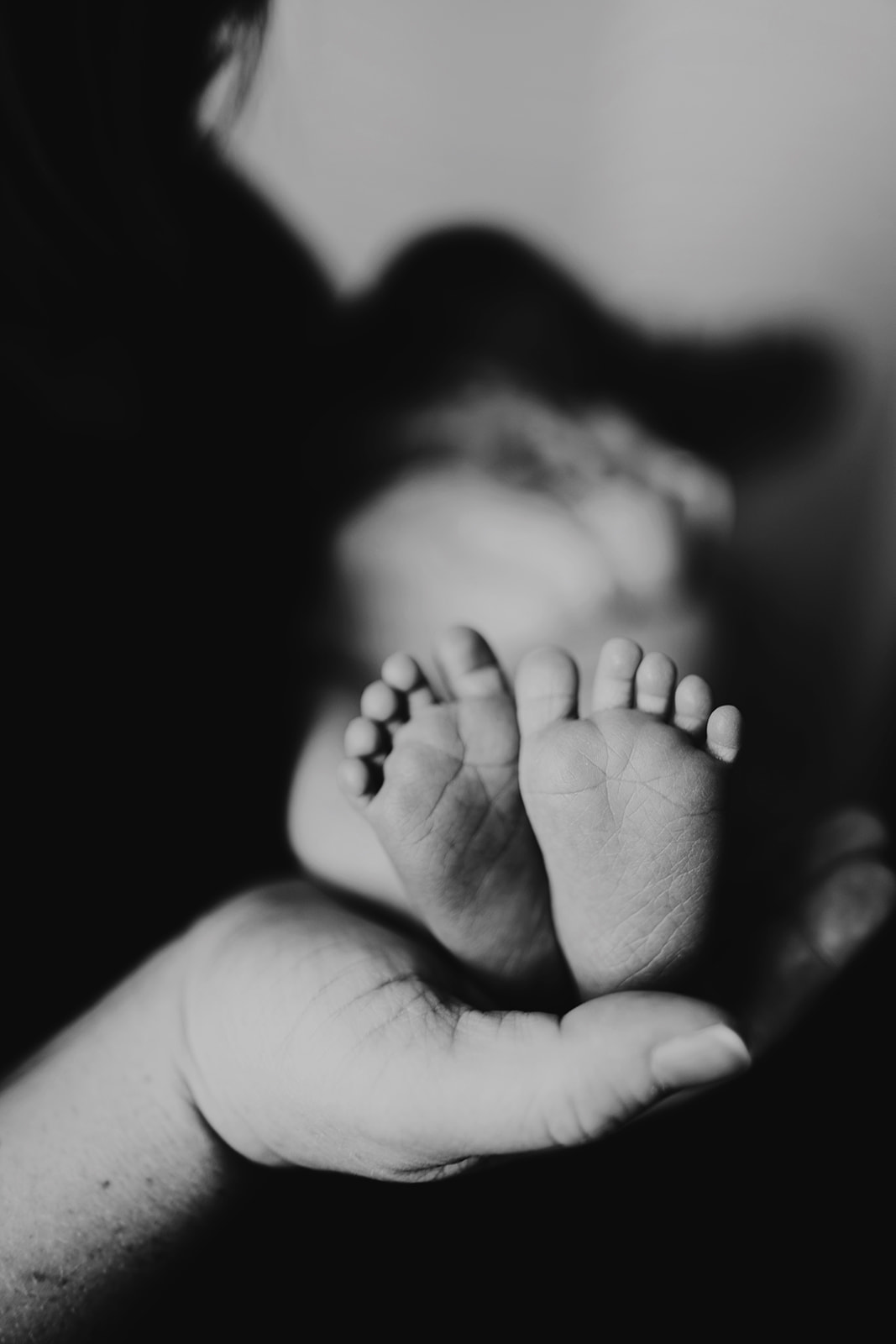 Mother cradles newborn baby's feet in her hand, black and white lifestyle session newborn photo