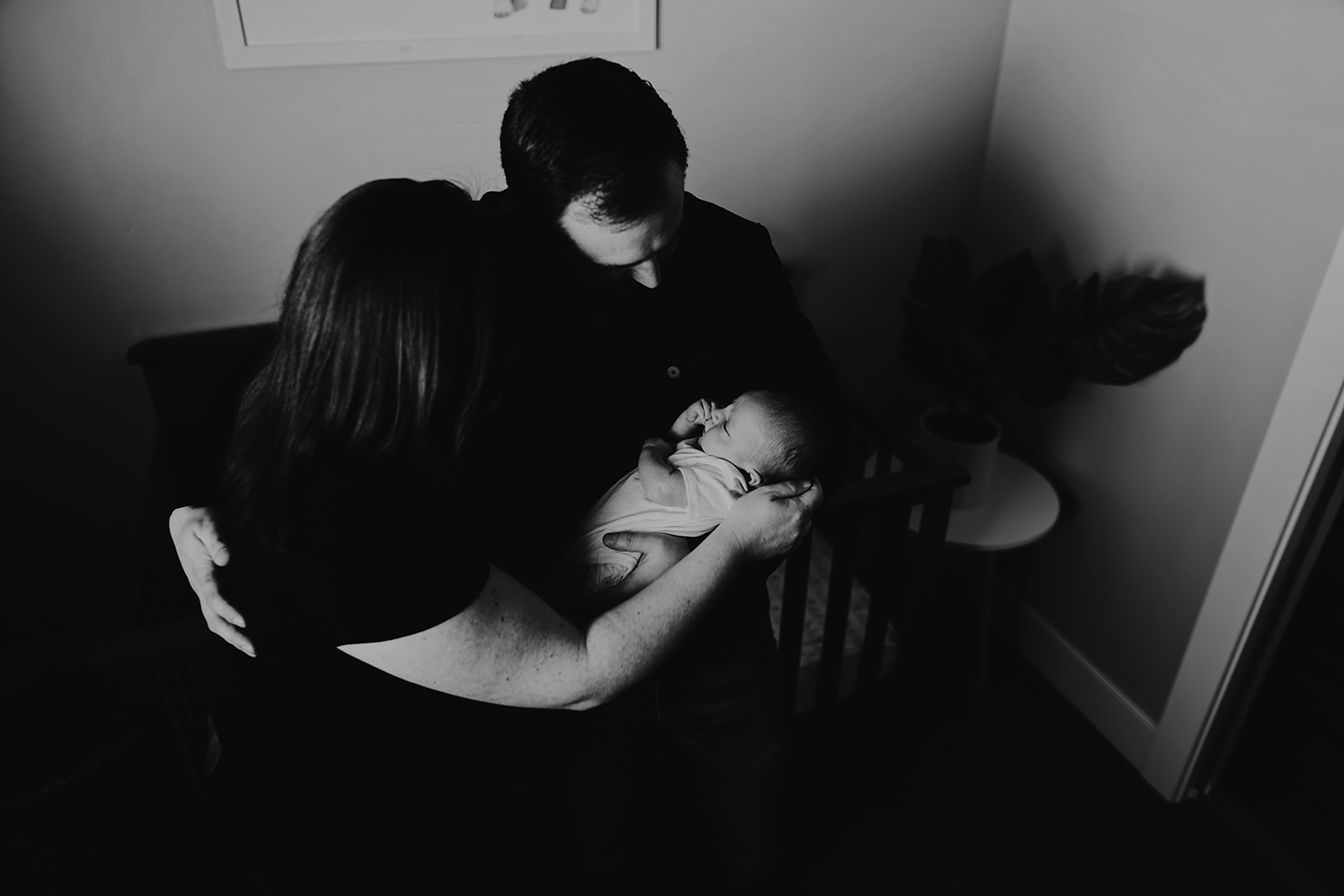 Black and white photo of mom and dad holding their newborn in front of his crib