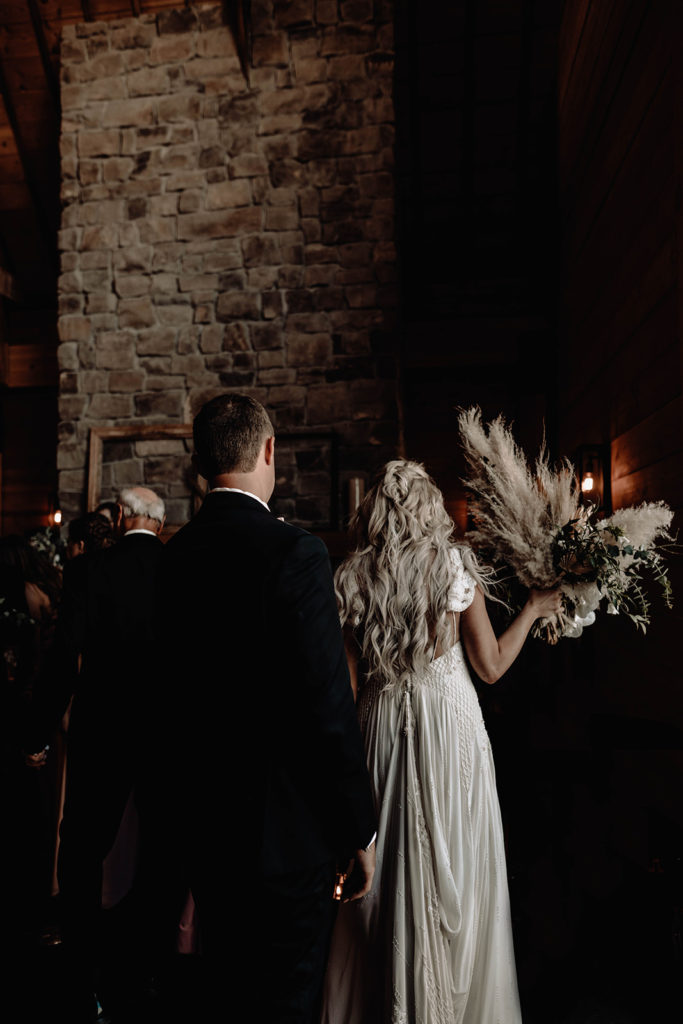 Dark and moody photo of bride and groom heading to their sweetheart table with Amber Everly Designs bouquet.
