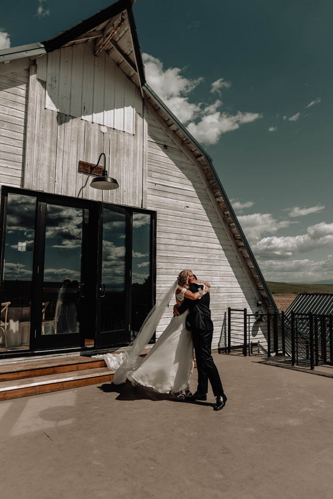 Bride and groom hug each other during their first look with the Foster Creek farm barn in the background