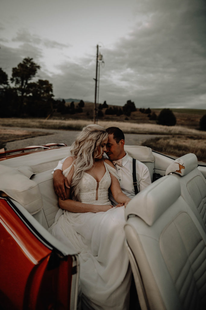 Bride and groom snuggle in the backseat of their vintage getaway car