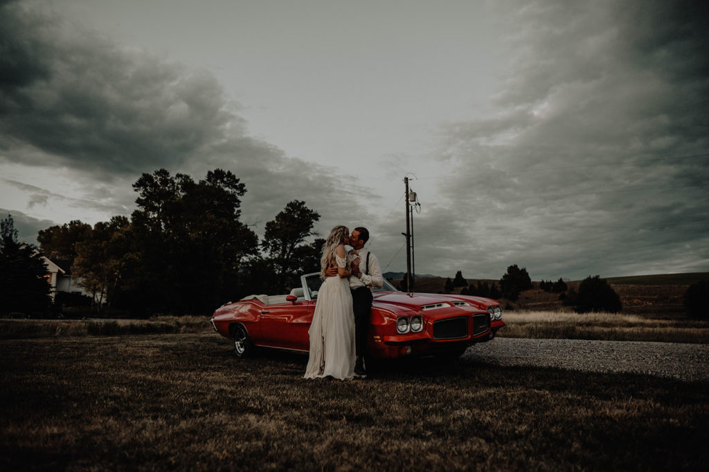 Newlyweds kissing on the hood of their vintage getaway car after their Foster Creek Farm wedding