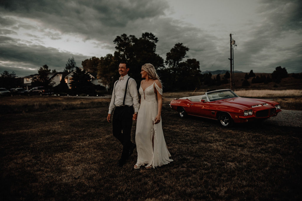 Bride and groom walk towards the Foster Creek Farm wedding reception with their vintage getaway car in the background.
