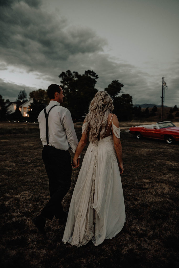 Bride and groom walking away from the camera towards their vintage getaway car