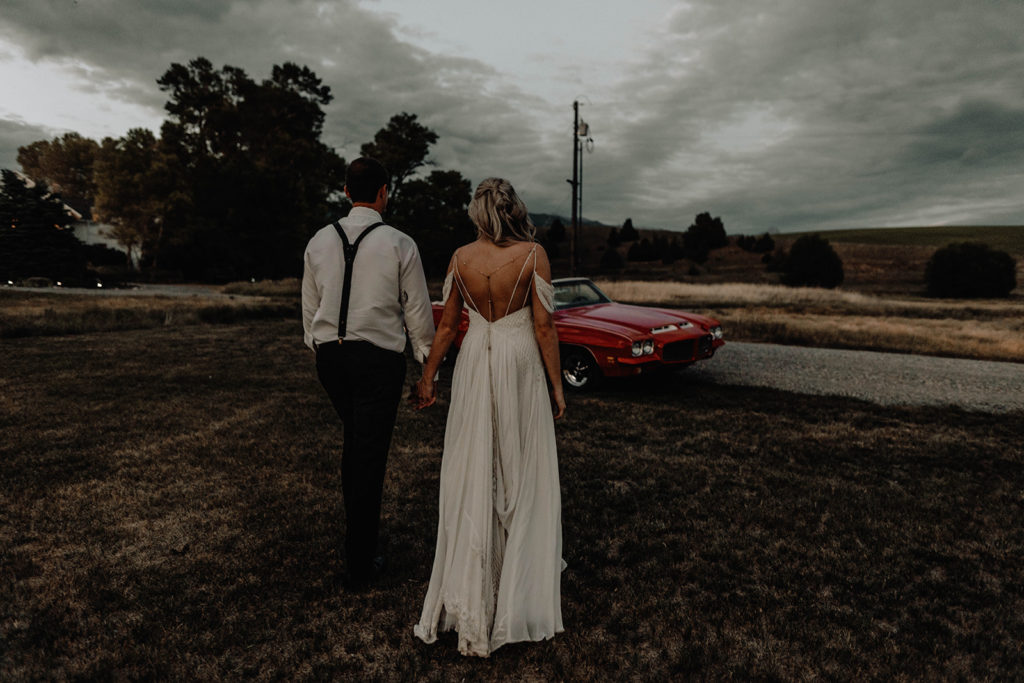 Photo of newlywed bride and groom holding hands towards their vintage getaway car during their Foster Creek Farm wedding