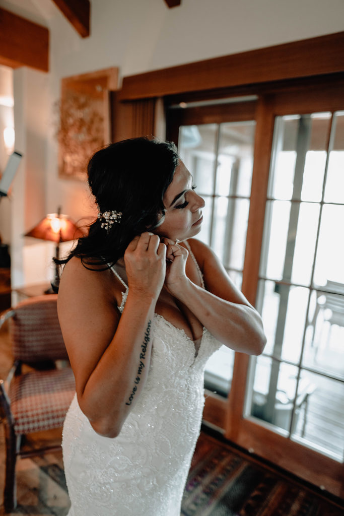 Bride puts on her earrings as she gets ready for her wedding ceremony in her Tamarack cabin