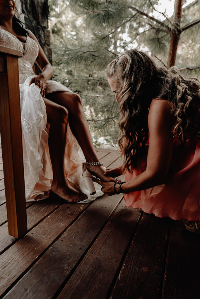 Future sister-in-law helps the bride put on her shoes before the wedding ceremony