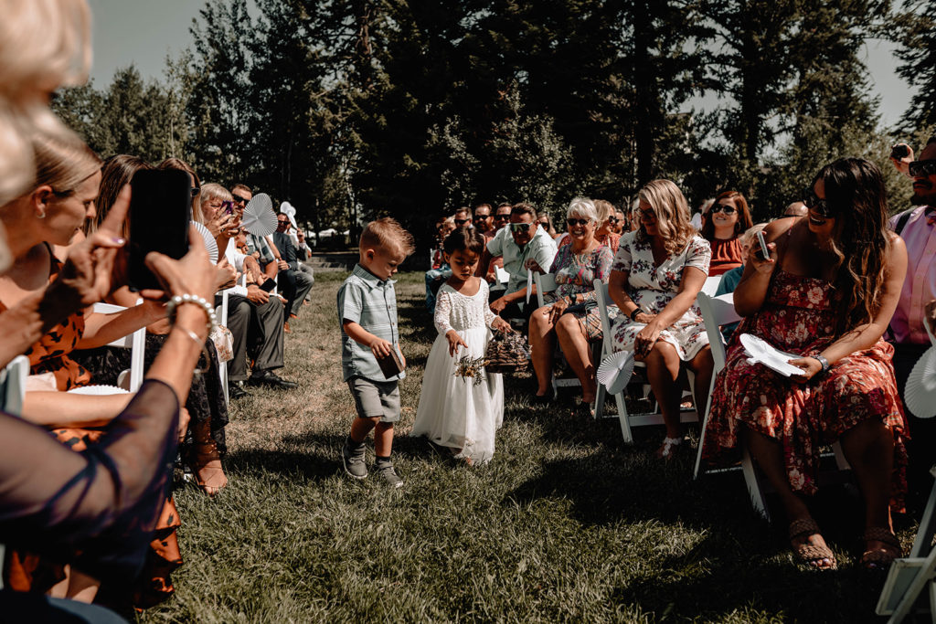 Flower girl and ring bearer walk down the aisle together with guests taking photos during a Tamarack Resort Wedding