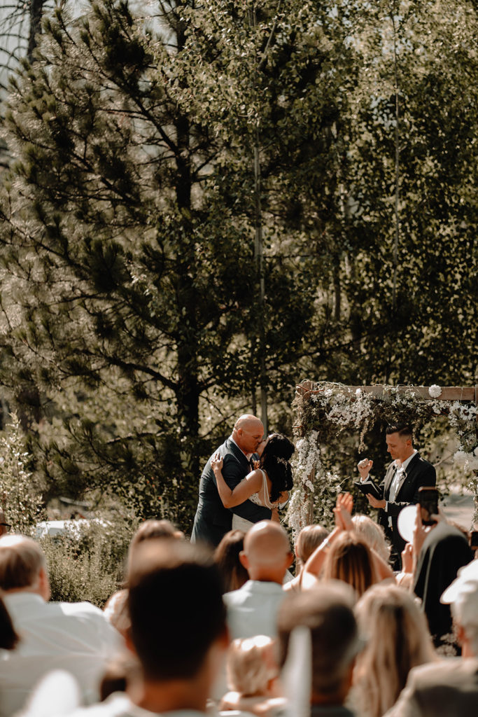 Bride and groom share their first kiss together as the best man and officiant fist pumps behind them