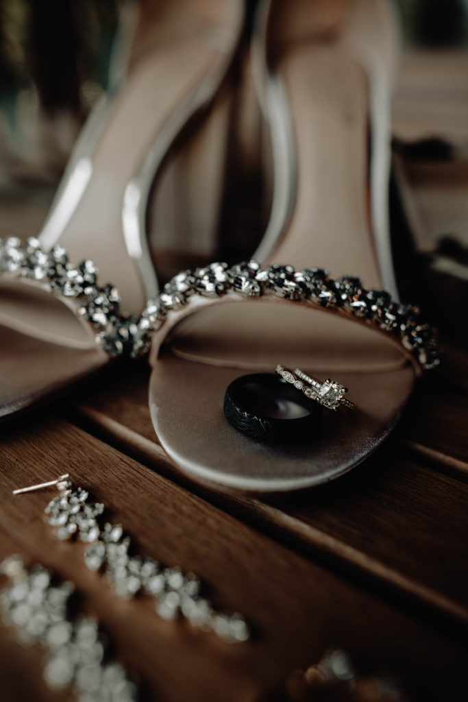 Detail shot of bride's shoes with engagement ring and wedding bands on a Tamarack cabin table 