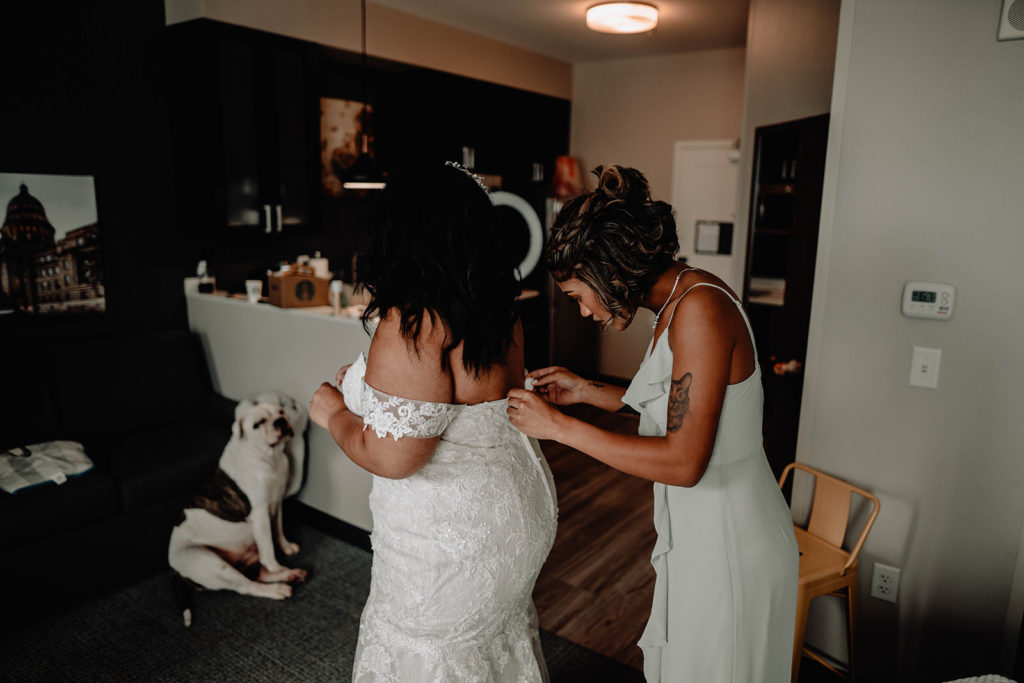 Maid of Honor laces up the bride into her wedding gown as they get ready for the day at the downtown Boise Residence Inn