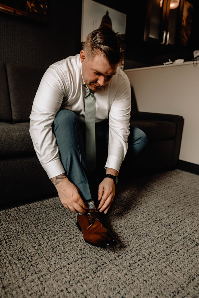 Groom sits on the hotel couch and adjusts his shoes as he gets ready for the wedding day