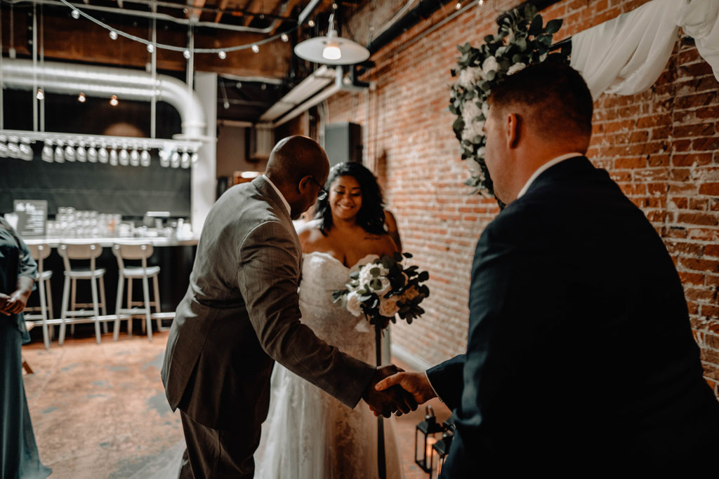 Father of the bride delivers his daughter to her groom at the end of the aisle in the downtown boise wedding venue beside bardenay