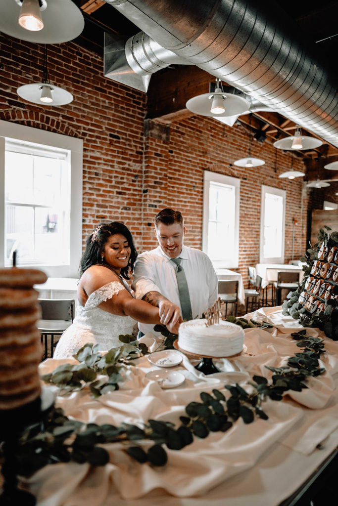 Bride and groom begin cutting their pastry perfections wedding cake in downtown Boise wedding venue, beside Bardenay